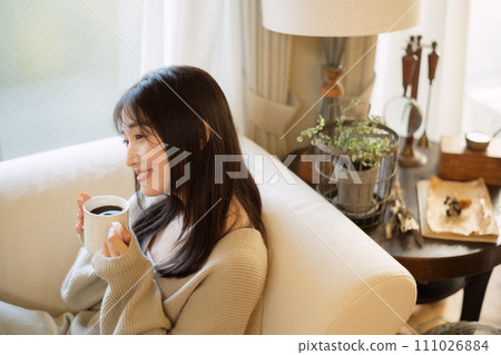 A woman drinking coffee while relaxing on a sofa 111026884