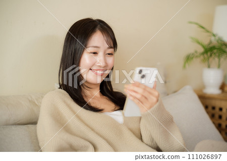 一位女士在房間的床上看著她的智慧型手機 111026897