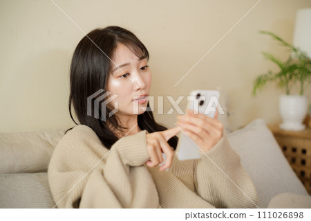 A woman looking at her smartphone on the bed in her room A woman looking at her smartphone on the bed in her room 111026898