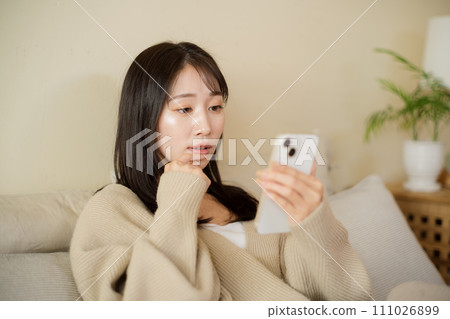 A woman looking at her smartphone on the bed in her room A woman looking at her smartphone on the bed in her room 111026899