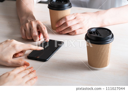 兩個人一邊喝飲料一邊指著智慧型手機 兩個人一邊喝飲料一邊指著智慧型手機 111027044