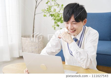 High school boy watching video on laptop in living room High school boy watching video on laptop in living room 111027543