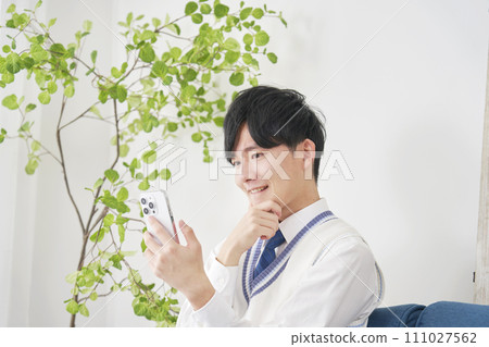 High school boy using his smartphone while thinking in the living room High school boy using his smartphone while thinking in the living room 111027562
