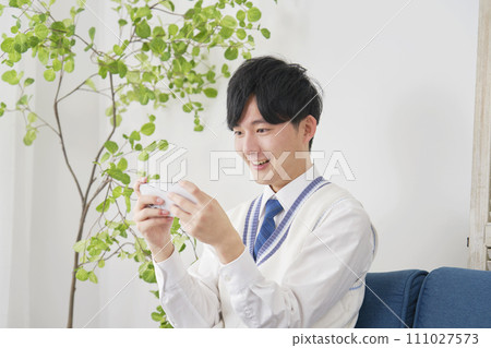 High school boy watching video on smartphone in living room High school boy watching video on smartphone in living room 111027573