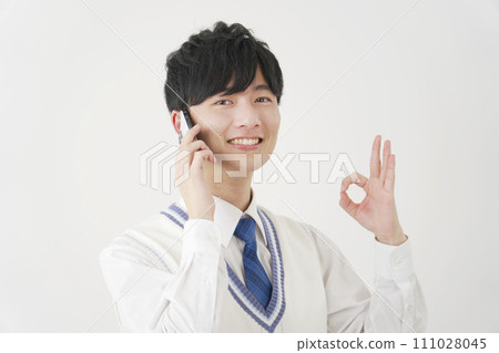 High school boy giving OK sign while calling on smartphone, white background 111028045