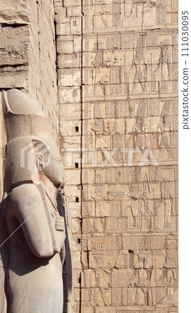 Pharaoh statue and stone wall with hieroglyphs in Karnak Temple, Luxor. Ancient Rameses II statue in Karnak Temple Complex, Luxor (ancient Thebes), Egypt, North Africa 111030095