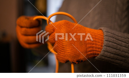 A hand's of a man in orange work gloves untangle orange wire 111031359