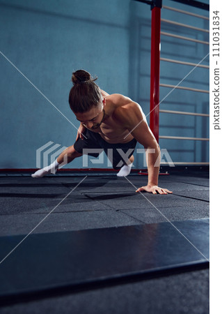 Young man with sportive, muscular, strong body training shirtless, doing one arm push ups in gym Young man with sportive, muscular, strong body training shirtless, doing one arm push ups in gym 111031834