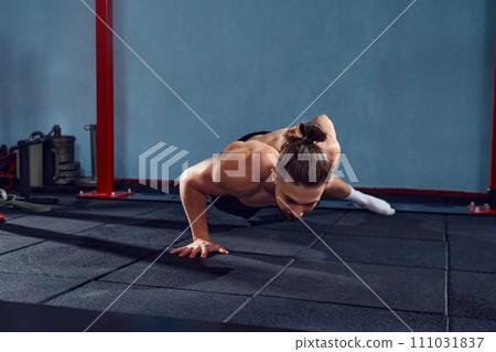 Young man with sportive, muscular, strong body training shirtless, doing one arm push ups in gym Young man with sportive, muscular, strong body training shirtless, doing one arm push ups in gym 111031837