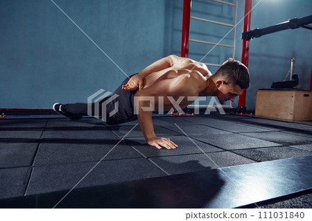 Young man with sportive, muscular, strong body training shirtless, doing one arm push ups in gym 111031840