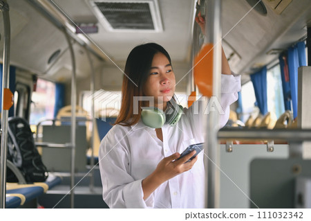 Attractive young woman standing in bus and using smart phone during her morning commute 111032342