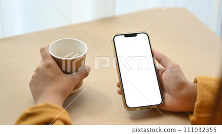 Closeup woman using mobile phone and drinking coffee at desk. Empty screen for application advertising 111032355