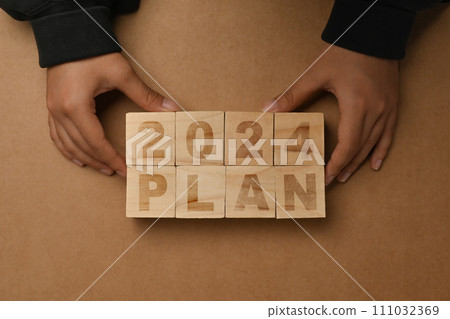 Hand arranging wooden cubes with 2024 PLAN text on brown background. Business plan concept 111032369