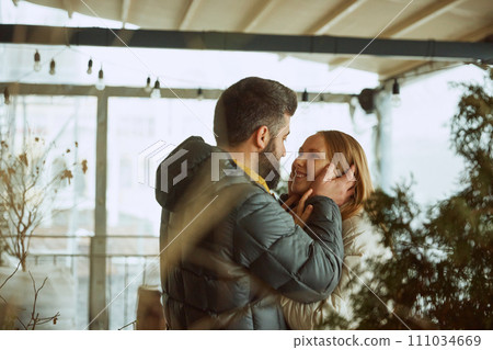 Young man and woman stands outdoor and with love and tenderness looks to each other dressed in winter coats. Warm relationships. Young man and woman stands outdoor and with love and tenderness looks to each other dressed in winter coats. Warm relationships. 111034669