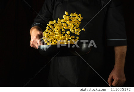 The chef throws pasta in a frying pan. Italian cuisine or shell-type pasta. Place for recipe or menu on black background The chef throws pasta in a frying pan. Italian cuisine or shell-type pasta. Place for recipe or menu on black background 111035172