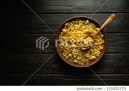 A plate of raw shell-type pasta and a spoon on an antique table before cooking. Place for recipe or menu on dark background 111035173