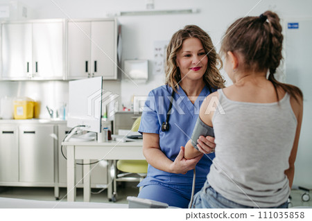 Doctor examining young girl, measuring blood pressure, using medical blood pressure monitor. Concept of preventive health care for children. 111035858