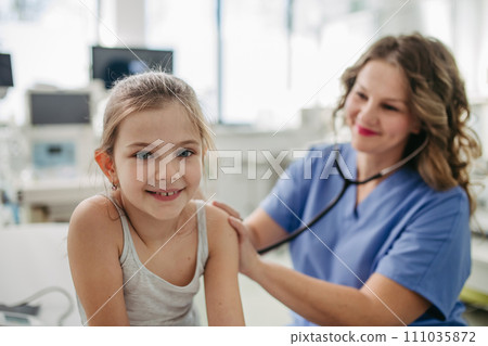 Orthopedist examines the spine, posture, and spinal deformities of little girl. Girl visiting paediatrician for annual preventive exam. Concept of preventive health care for children. 111035872