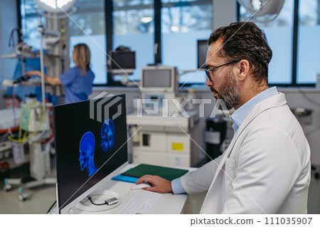 Portrait of ER doctor in hospital working in emergency room. Healthcare worker looking at MRI scan on medical computer in emergency room. Portrait of ER doctor in hospital working in emergency room. Healthcare worker looking at MRI scan on medical computer in emergency room. 111035907