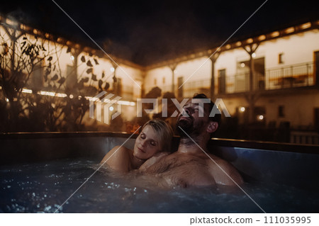 Beautiful mature couple relaxing in outdoor hot tub, enjoying romantic wellness weekend in spa. Concept of Valentine's Day. 111035995