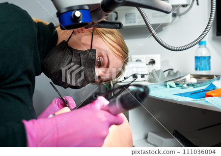 Close-up of female dentist who is learning to treat teeth on human head mannequin. Medical student in protective mask and sterile gloves holding a dental drill. Stomatology and orthodontics concept. Close-up of female dentist who is learning to treat teeth on human head mannequin. Medical student in protective mask and sterile gloves holding a dental drill. Stomatology and orthodontics concept. 111036004