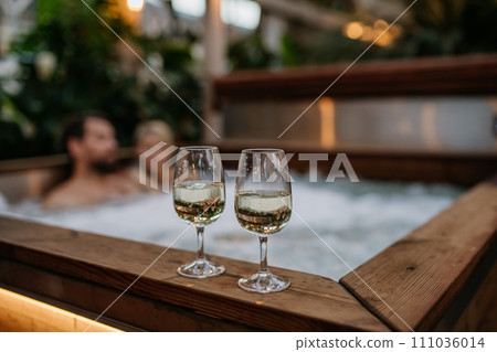 Two wine glasses on hot tub, couple relaxing, enjoying romantic wellness weekend in spa. Concept of Valentine's Day. Two wine glasses on hot tub, couple relaxing, enjoying romantic wellness weekend in spa. Concept of Valentine's Day. 111036014