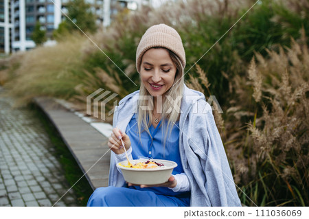 Nurse having healthy lunch, snack in front of hospital building, taking break from work. Importance of breaks in healthcare. 111036069