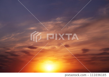 Beautiful colorful dramatic sky with clouds at sunset. Bright orange setting sun low on the horizon. Cirrus clouds change color from blue to yellow to red. Stunning backdrop, gorgeous scenery. 111036185