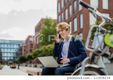 Businessman, freelancer or manager working outdoors in city park. Man with laptop on knees having video call. Concept of working remotely. 111036234