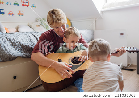Father teaching boy to play on guitar. Son having fun in their room with dad, playing guitar and singing together. Concept of Father's Day, and fatherly love. 111036305
