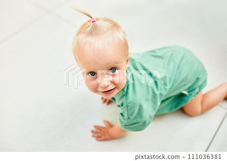 Small cute child crawling on the floor in a public place, shopping mall. Tiny blonde girl in green clothes smiling and having fun with mom while shopping. Funny weekend, happy childhood. Small cute child crawling on the floor in a public place, shopping mall. Tiny blonde girl in green clothes smiling and having fun with mom while shopping. Funny weekend, happy childhood. 111036381