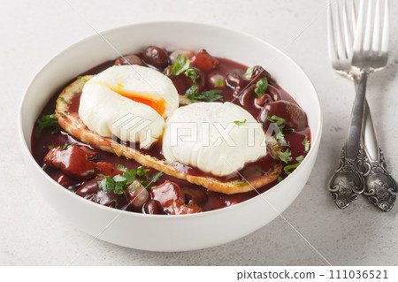 Oeufs en meurette Burgundy poached eggs with toast in red wine sauce with mushrooms, onions and bacon close-up in a plate. Horizontal Oeufs en meurette Burgundy poached eggs with toast in red wine sauce with mushrooms, onions and bacon close-up in a plate. Horizontal 111036521