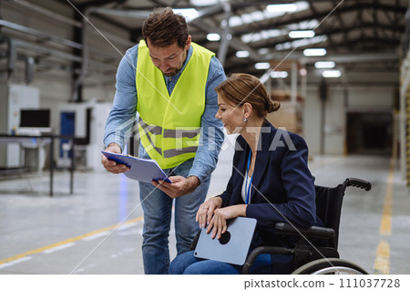 Portrait of female manager in wheelchair working in warehouse, talking with logistics employee. Concept of workers with disabilities, accessible workplace for employees with mobility impairment. Portrait of female manager in wheelchair working in warehouse, talking with logistics employee. Concept of workers with disabilities, accessible workplace for employees with mobility impairment. 111037728