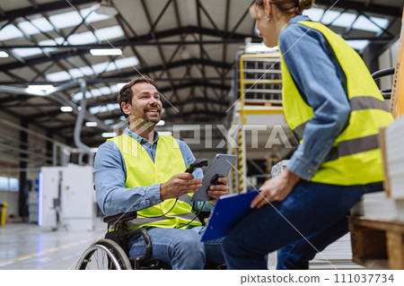 Portrait of man in wheelchair working in modern industrial factory, talking with female coworker. Concept of workers with disabilities, accessible workplace for employees with mobility impairment. Portrait of man in wheelchair working in modern industrial factory, talking with female coworker. Concept of workers with disabilities, accessible workplace for employees with mobility impairment. 111037734