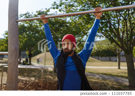 Handsome man exercises outdoors at an urban outdoor gym. Exercising after work for good mental health, physical health, and relieving stress and boost mood. Handsome man exercises outdoors at an urban outdoor gym. Exercising after work for good mental health, physical health, and relieving stress and boost mood. 111037785