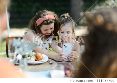 Cousins taking a selfie at a family garden party. Family reunion at garden barbecue party. Cousins taking a selfie at a family garden party. Family reunion at garden barbecue party. 111037799