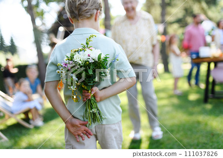 Beautiful senior birthday woman receiving flowers from grandchildren. Concept of garden birthday party for elderly woman. 111037826