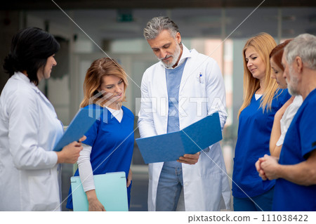 Team of doctors discussing unique medical case, walking across corridor. Colleagues, doctors team discussing patients diagnosis. 111038422
