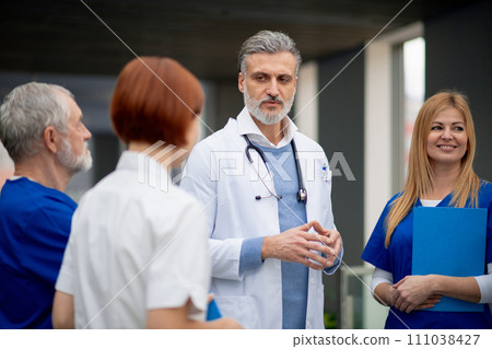 Team of doctors discussing unique medical case, walking across corridor. Colleagues, doctors team discussing patients diagnosis. Team of doctors discussing unique medical case, walking across corridor. Colleagues, doctors team discussing patients diagnosis. 111038427