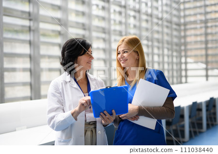 Two female doctors discussing test results, patients diagnosis. walking across corridor. Women in medicine science 111038440