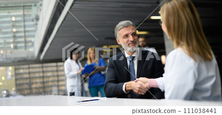 Doctor talking to pharmaceutical sales representative, shaking hands. Hospital manager talking with female doctor. Banner with copyspace. Doctor talking to pharmaceutical sales representative, shaking hands. Hospital manager talking with female doctor. Banner with copyspace. 111038441