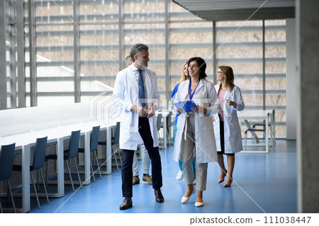 Team of doctors discussing test results, walking across corridor. Colleagues discussing patients diagnosis. 111038447