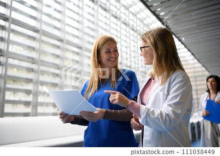 Two female doctors discussing test results, patients diagnosis. walking across corridor. Women in medicine science 111038449