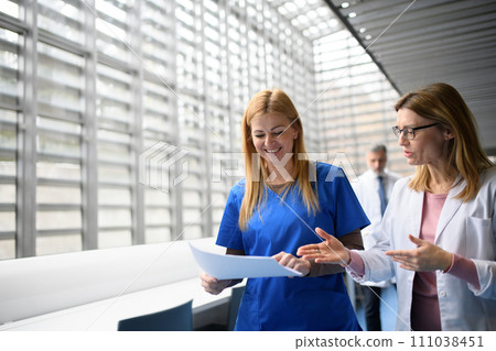 Two female doctors discussing test results, patients diagnosis. walking across corridor. Women in medicine science Two female doctors discussing test results, patients diagnosis. walking across corridor. Women in medicine science 111038451