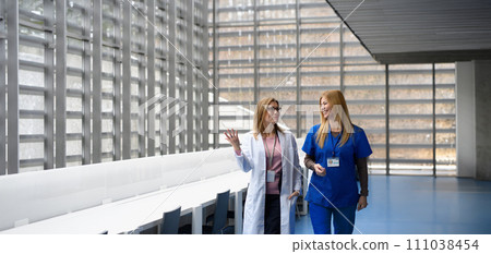Two female doctors discussing test results, patients diagnosis. walking across corridor. Women in medicine science Two female doctors discussing test results, patients diagnosis. walking across corridor. Women in medicine science 111038454