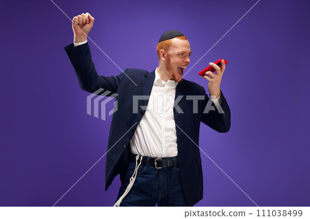 Young Jewish smiling man emotionally recording voice message against purple studio background 111038499