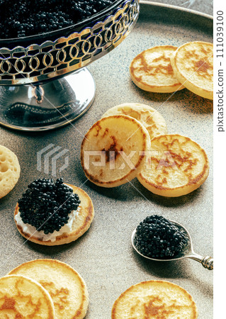Mini crepes with black caviar and cream cheese, on a festive dish, mini pancakes 111039100