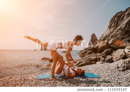 Woman sea yoga. Two happy women practicing yoga on the beach with ocean and rock mountains. Motivation and inspirational fit and exercising. Healthy lifestyle outdoors in nature, fitness concept. Woman sea yoga. Two happy women practicing yoga on the beach with ocean and rock mountains. Motivation and inspirational fit and exercising. Healthy lifestyle outdoors in nature, fitness concept. 111039187