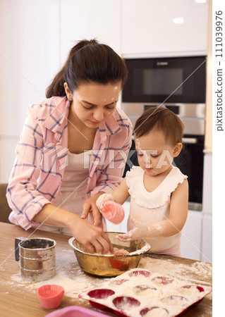 mother and little baby girl preparing the dough in the kitchen, bake cookies. happy time together mother and little baby girl preparing the dough in the kitchen, bake cookies. happy time together 111039976
