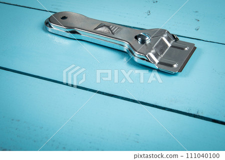 Glass ceramic scraper on a blue wooden texture background. 111040100